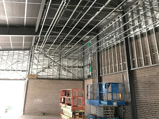 College building: steel roof framing with scissor lifts on the floor