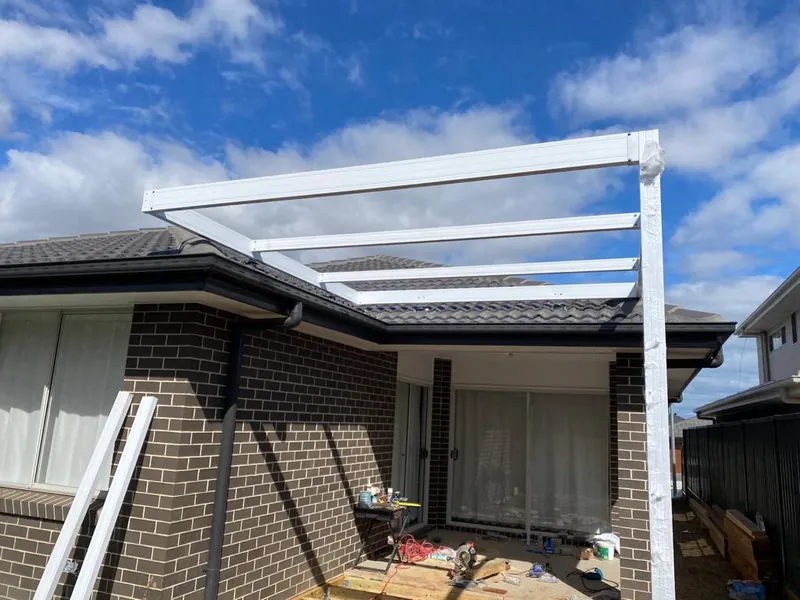 White posts and beams of a new pergola against a brick home